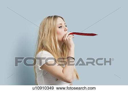 Young woman blowing party blower against light blue background View Large Photo Image Stock Photo - Young woman blowing party blower against light blue background. Fotosearch