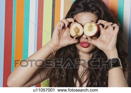 Stock Image - Young woman covering her eyes with peach against striped background. Fotosearch