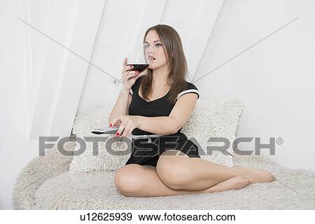 Young woman having a drink on sofa while changing channels with remote control View Large Photo Image Stock Photo - Young woman having a drink on sofa while changing channels with remote control. Fotosearch