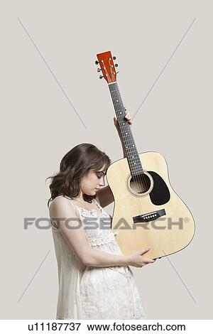Young woman holding guitar against gray background View Large Photo Image Stock Photo - Young woman holding guitar against gray background. Fotosearch