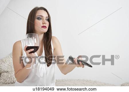 Young woman holding wineglass while changing channels with remote control View Large Photo Image Stock Photo - Young woman holding wineglass while changing channels with remote control. Fotosearch