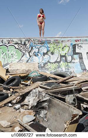 Stock Photo - Young woman in bikini standing on graffiti wall with garbage in foreground. Fotosearch