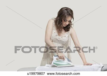 Stock Photo - Young woman ironing shirt against gray background. Fotosearch