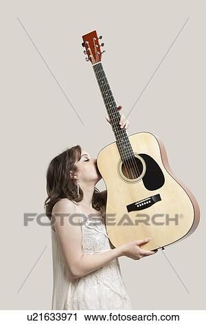 Young woman kissing guitar against gray background View Large Photo Image Stock Image - Young woman kissing guitar against gray background. Fotosearch