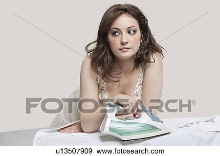 Young woman looking away while ironing shirt over gray background View Large Photo Image Stock Photo - Young woman looking away while ironing shirt over gray background. Fotosearch