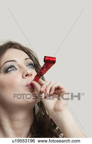 Young woman looking up while blowing party puffer against gray background View Large Photo Image Stock Photograph - Young woman looking up while blowing party puffer against gray background. Fotosearch
