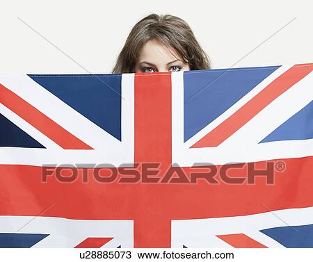 Stock Image - Young woman peeking over British flag against gray background. Fotosearch