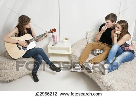 Young woman playing guitar with friends sitting on sofa View Large Photo Image Stock Image - Young woman playing guitar with friends sitting on sofa. Fotosearch