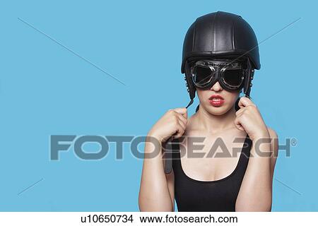 Young woman wearing nostalgic helmet and goggles against blue background View Large Photo Image Picture - Young woman wearing nostalgic helmet and goggles against blue background. Fotosearch