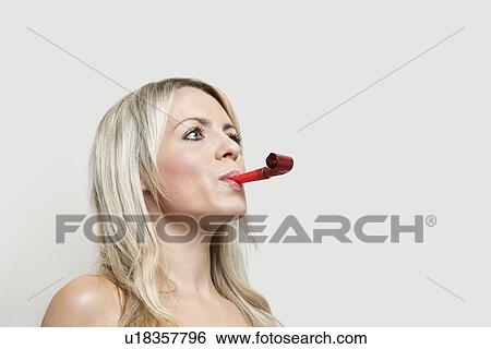 Young woman with party blower looking away over gray background View Large Photo Image Stock Photograph - Young woman with party blower looking away over gray background. Fotosearch