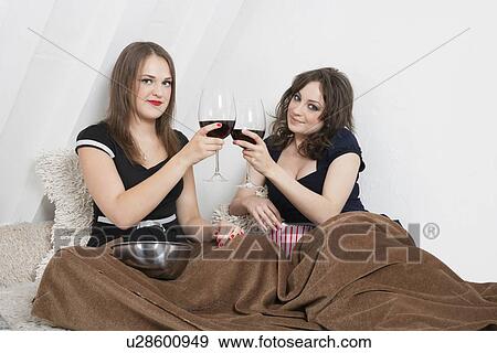 Stock Photo - Young women toasting with wine glasses in bed. Fotosearch