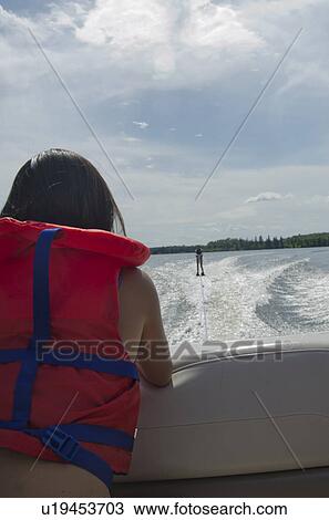 Stock Image - Girl looking at a person waterskiing in a lake, Lake of the Woods, Ontario, Canada. Fotosearch