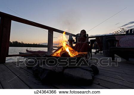 Stock Photograph - Girl sitting near a campfire, Lake of the Woods, Ontario, Canada. Fotosearch