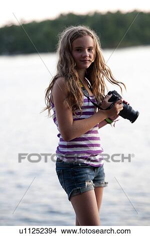 Picture - Girl standing at the lakeside with a digital camera, Lake of the Woods, Ontario, Canada. Fotosearch