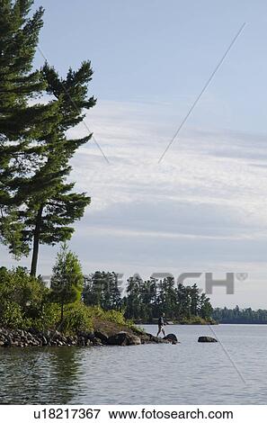 Stock Photo - Man fishing at lakeside, Lake of the Woods, Ontario, Canada. Fotosearch