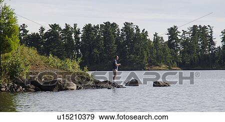 Stock Photo - Man standing at the lakeside fishing, Lake of the Woods, Ontario, Canada. Fotosearch