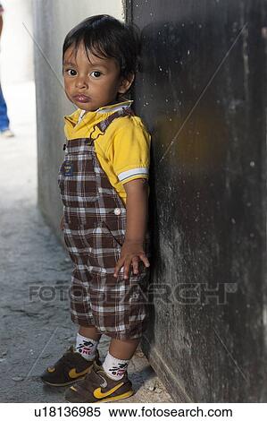 Stock Photography - Portrait of a boy standing in front of a closed door, Colonia Bethania, Guatemala City, Guatemala. Fotosearch