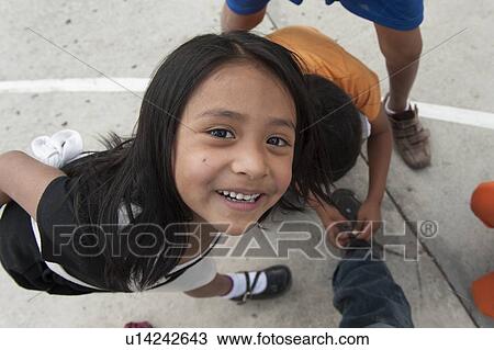 Stock Image - Portrait of a girl smiling while another boy tying shoelace of his friend, Colonia Bethania, Guatemala City, Guatemala. Fotosearch