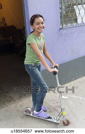 Stock Photo - Portrait of happy girl riding a push scooter, Colonia Bethania, Guatemala City, Guatemala. Fotosearch