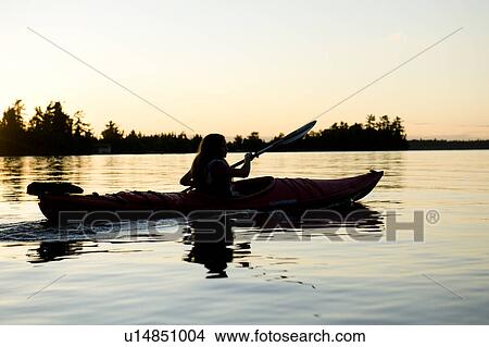 Picture - Silhouette of a girl kayaking in a lake, Lake of the Woods, Ontario, Canada. Fotosearch