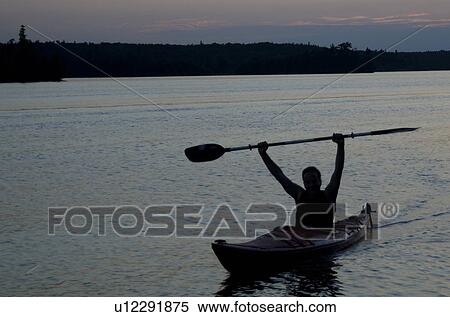 Stock Photography - Silhouette of a man kayaking in a lake, Lake of the Woods, Ontario, Canada. Fotosearch