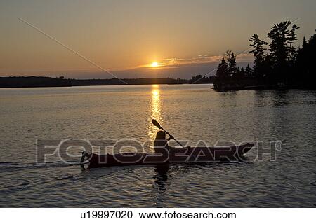 Stock Image - Silhouette of a person rowing a boat, Lake of the Woods, Ontario, Canada. Fotosearch