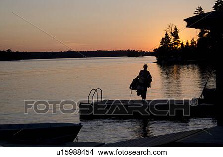 Silhouette of a person walking on a boardwalk, Lake of the Woods, Ontario, Canada View Large Photo Image Picture - Silhouette of a person walking on a boardwalk, Lake of the Woods, Ontario, Canada. Fotosearch