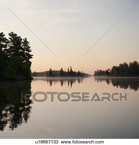 Stock Image - Silhouette of trees at the lakeside, Lake of the Woods, Ontario, Canada. Fotosearch