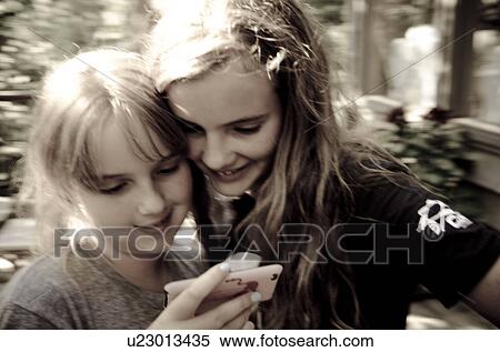 Two girls looking at a mobile phone, Lake of the Woods, Ontario, Canada View Large Photo Image Stock Photography - Two girls looking at a mobile phone, Lake of the Woods, Ontario, Canada. Fotosearch