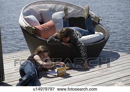 Stock Photo - Woman reading a book with her daughter playing on wooden floor, Lake of the Woods, Ontario, Canada. Fotosearch