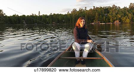 Stock Image - Woman rowing a boat in a lake, Lake of the Woods, Ontario, Canada. Fotosearch