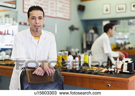 Stock Image - Barber standing at chair in shop. Fotosearch