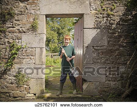 Stock Image - Boy carrying shovel in backyard. Fotosearch