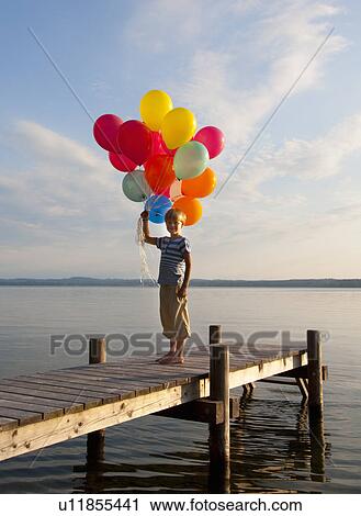 Stock Image - Boy holding balloons on wooden pier. Fotosearch