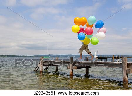 Boy holding balloons on wooden pier View Large Photo Image Stock Image - Boy holding balloons on wooden pier. Fotosearch