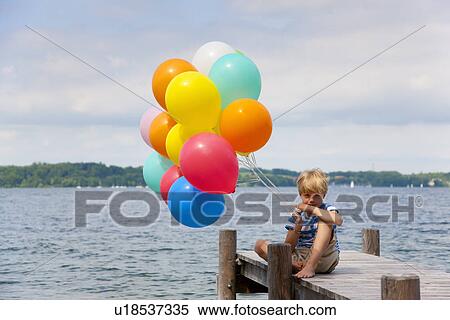 Stock Photography - Boy holding balloons on wooden pier. Fotosearch