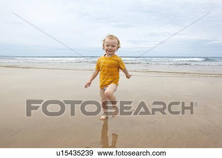 Stock Photo - Boy walking in waves on beach. Fotosearch