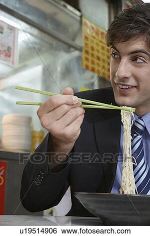 Stock Photograph - Businessman eating noodles in cafe. Fotosearch