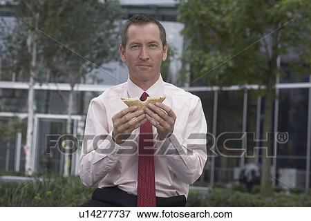 Stock Photo - Businessman eating sandwich in city park. Fotosearch