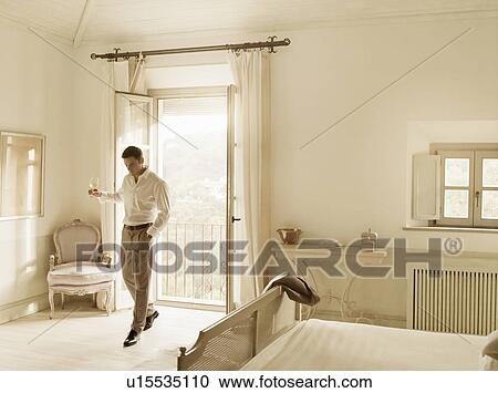 Stock Image - Businessman having wine in bedroom. Fotosearch