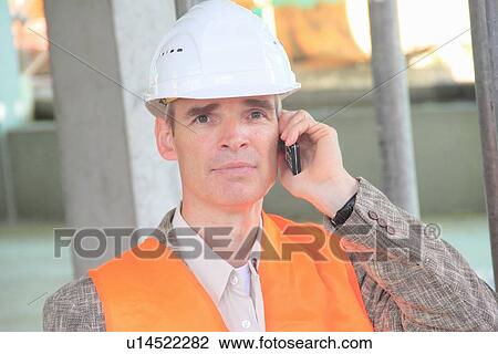 Stock Image - Businessman in hard hat on cell phone. Fotosearch