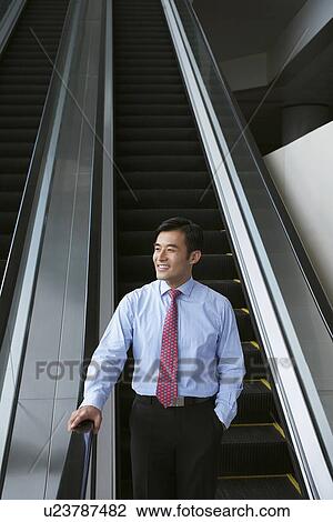 Stock Image - Businessman riding escalator in office. Fotosearch