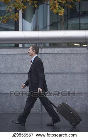 Stock Photo - Businessman rolling luggage outdoors. Fotosearch