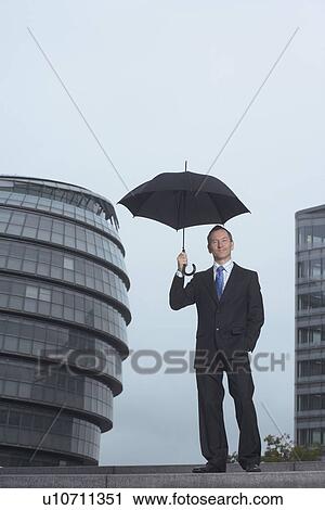 Stock Image - Businessman standing under umbrella. Fotosearch