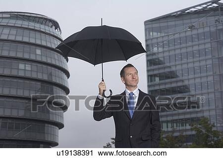 Businessman standing under umbrella View Large Photo Image Stock Image - Businessman standing under umbrella. Fotosearch