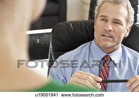 Stock Image - Businessman talking to colleague at desk. Fotosearch