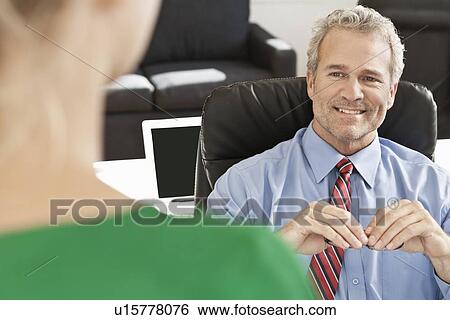 Businessman talking to colleague at desk View Large Photo Image Stock Photograph - Businessman talking to colleague at desk. Fotosearch