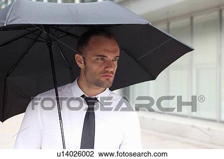 Stock Image - Businessman walking under umbrella. Fotosearch