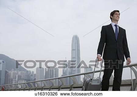 Businessman with luggage by urban bay View Large Photo Image Stock Photograph - Businessman with luggage by urban bay. Fotosearch