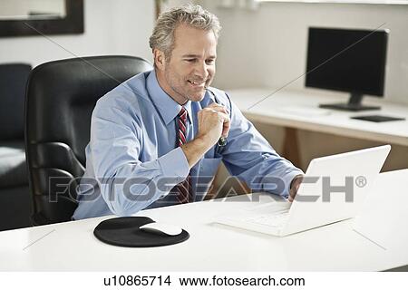 Picture - Businessman working on laptop at desk. Fotosearch